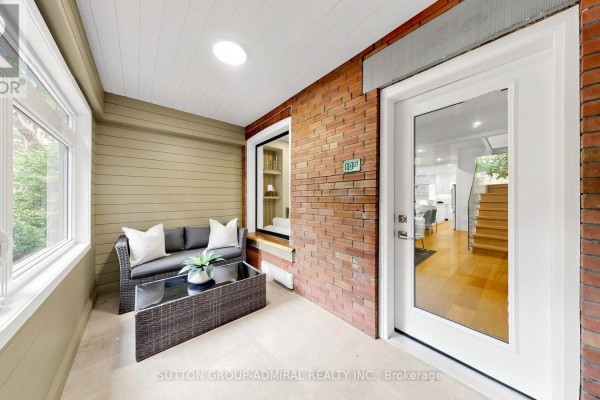 Living room with large window showing brick exterior, fireplace, and stairs. - 109 Fermanagh Avenue, Toronto