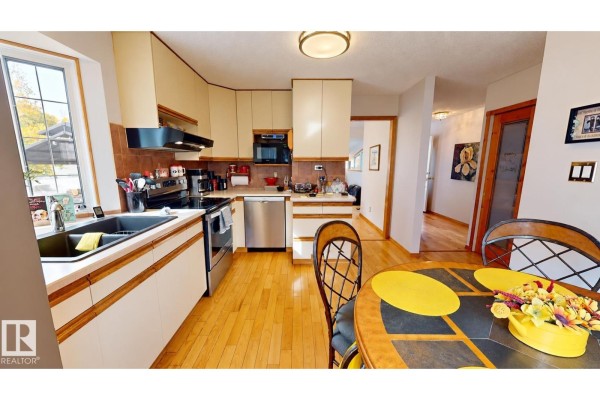 Panoramic view of a kitchen with wood floors, stainless steel appliances, and hallway access. - 109 Galen Pl, Sherwood Park