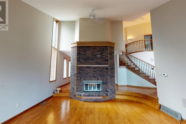 Living room with brick fireplace, hardwood floors, and curved staircase - 109 Greenview Ln Sault Ste Marie