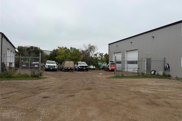 View of the property's gravel lot with several vehicles parked, enclosed by a chain-link fence. - 109 Industrial Drive, Brandon