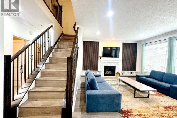 Living room with a white fireplace, two blue sofas, a coffee table, and a staircase with dark wood railing. - 109 Kinniburgh Boulevard E Boulevard E, Chestermere