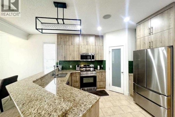 Kitchen with light wood cabinets, granite countertops, stainless steel appliances, and an island with seating. - 109 Kinniburgh Boulevard E Boulevard E, Chestermere