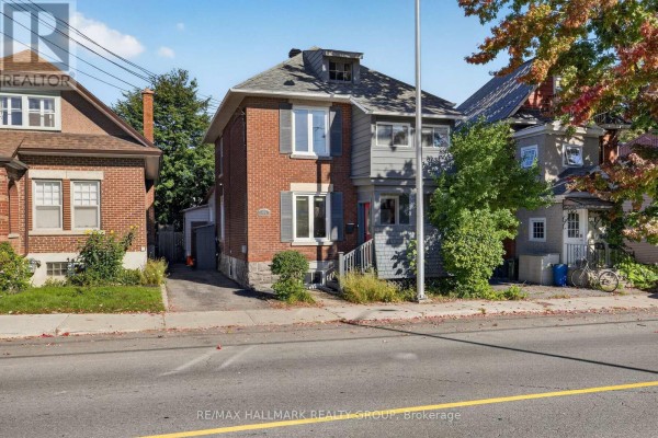 Exterior of a two-story red brick house with gray siding, shutters, and a pitched roof under a bright sky. - 109 Lees Avenue, Ottawa