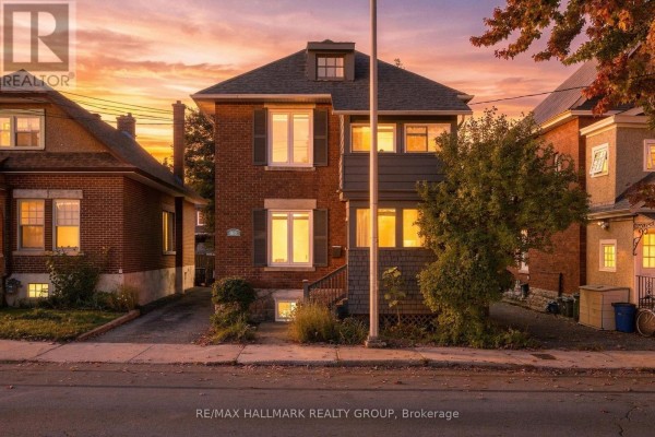 Exterior of a two-story red brick house with gray siding and illuminated windows at sunset. - 109 Lees Avenue, Ottawa