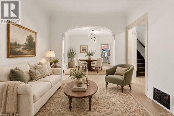 Living room with a beige sofa, green armchair, oval coffee table, and arched doorway to dining area. - 109 Macaulay Street E, Hamilton