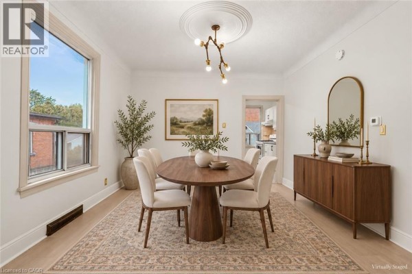 Dining room with oval wooden table, six cream chairs, wooden sideboard, and large window. - 109 Macaulay Street E, Hamilton