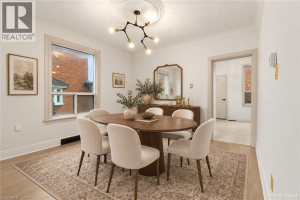 View of dining room with oval table, cream chairs, sideboard, and doorway to hallway. - 109 Macaulay Street E, Hamilton