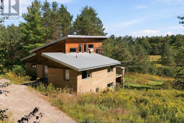 Side view of the house showing rammed earth walls, metal roof, and deck with glass railings. - 109 Mount Pleasant Road, Cramahe