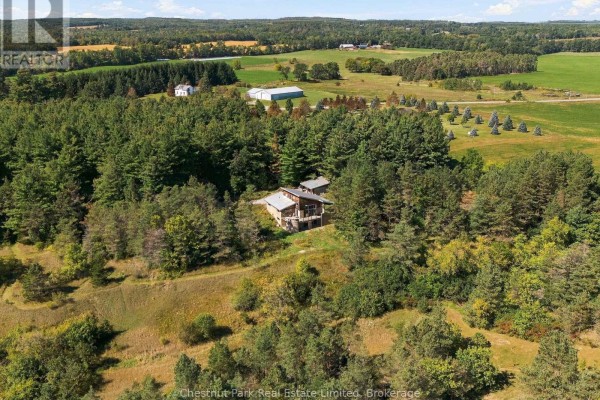 Aerial view of the property nestled in a forested area with fields and buildings in the distance. - 109 Mount Pleasant Road, Cramahe