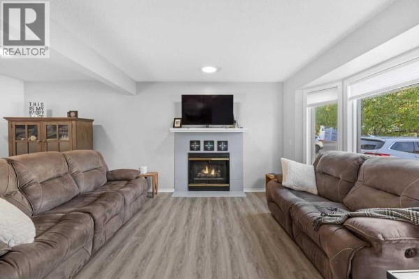 Living room with a gas fireplace, television, two large brown couches, and a bay window. - 109 Patina Park Sw, Calgary