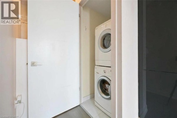 Stacked white washing machine and dryer in a small laundry closet with a white door. - 109 Wolseley Street Unit# 204, Toronto