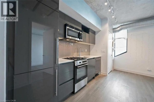 A compact kitchen with grey high-gloss cabinets, stainless steel appliances, and a tiled backsplash. - 109 Wolseley Street Unit# 204, Toronto