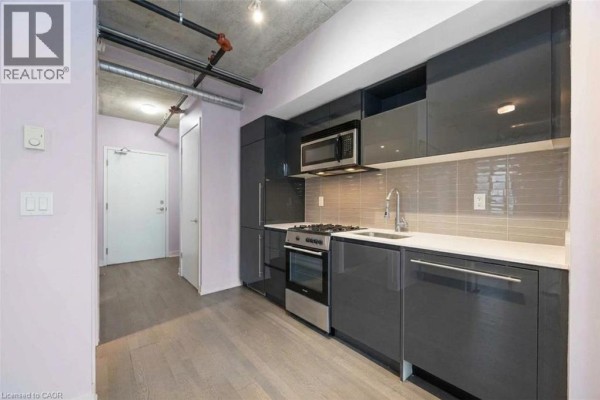 View of the kitchen area with grey cabinets, stainless steel appliances, and exposed industrial pipes on the ceiling. - 109 Wolseley Street Unit# 204, Toronto