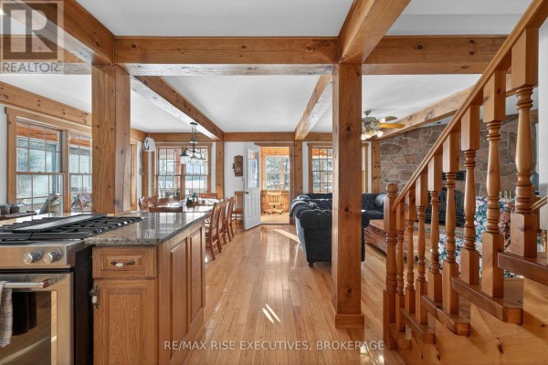 Open-concept living area with wood beams, stone fireplace, and wooden staircase. - 1093b Two Loon Lane, Frontenac