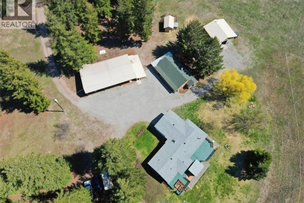 Aerial view of the large metal workshop with equipment inside, a small house, and a gravel driveway. - 1094 Highway 5a, Princeton