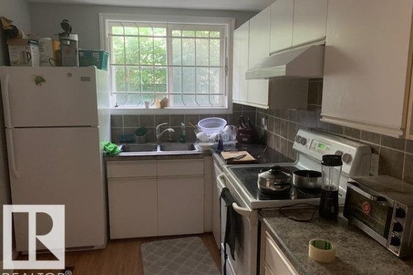 Kitchen with white refrigerator, stove, sink, and white cabinets overlooking a window. - 10965 96 St Nw Nw, Edmonton