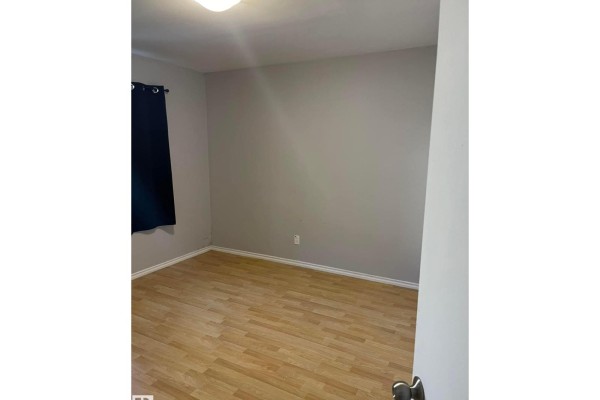 Empty bedroom with light wood floor, gray walls, and a dark curtain. - 10965 96 St Nw Nw, Edmonton