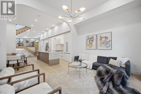 Living room with charcoal sofa, cream chairs, gold coffee table, and archway to kitchen. - 10a Holmstead Avenue, Toronto