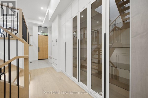 Interior hallway with light wood floors, light wood staircase, and a wall of white cabinets with glass doors. - 10a Holmstead Avenue, Toronto