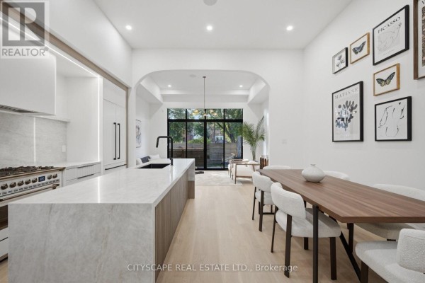 Modern kitchen with marble island and countertops, stainless steel range, and dining area with wooden table. - 10a Holmstead Avenue, Toronto
