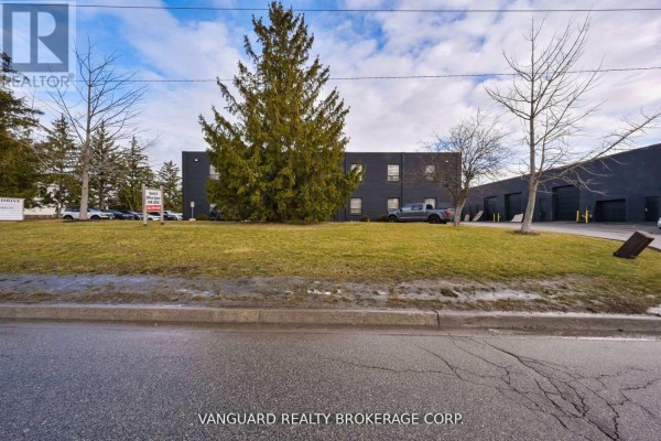 Exterior view of a dark brick commercial building with grassy area and driveway. - 10r-10f - 11 Holland Drive, Caledon