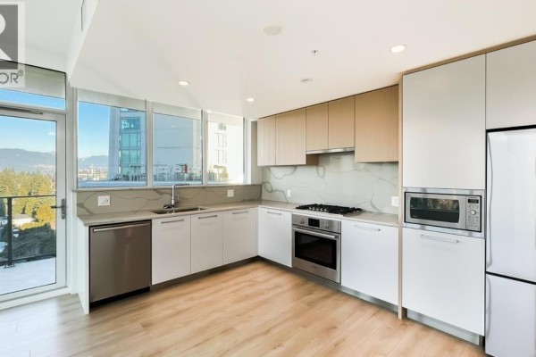 L-shaped kitchen with quartz countertops, stainless steel appliances, and light wood cabinetry. - 10xx 567 Clarke Road, Coquitlam