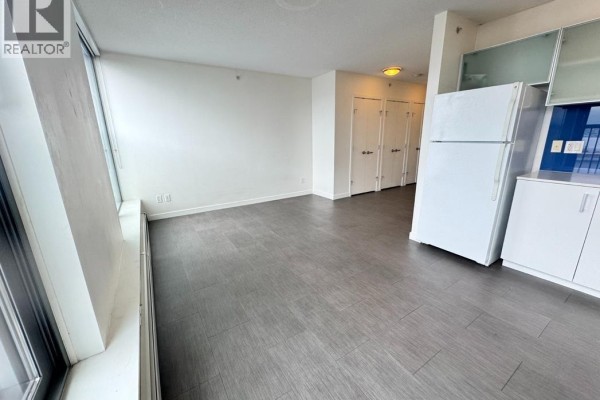 View of the apartment living area from the kitchen. White walls and grey flooring are present. - 10xx 66 W Cordova Street, Vancouver