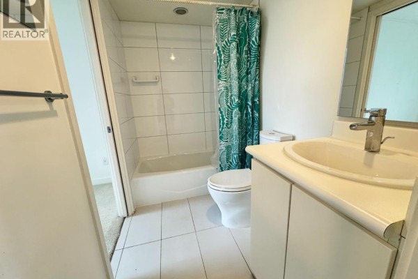 Apartment bathroom with a bathtub, toilet, and vanity. White tiles and a patterned shower curtain are visible. - 10xx 66 W Cordova Street, Vancouver