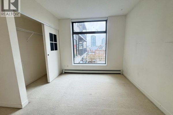 Apartment bedroom with carpeted floors and a large window offering a view of city buildings. - 10xx 66 W Cordova Street, Vancouver