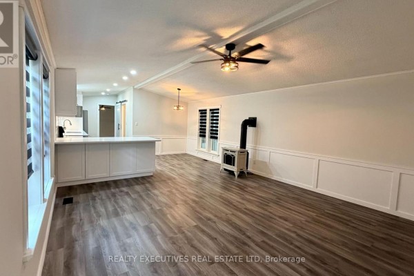 Living room and kitchen area with white cabinets, island, wood-look floors, and stove. - 11 - 10146 County 43 Road, North Dundas