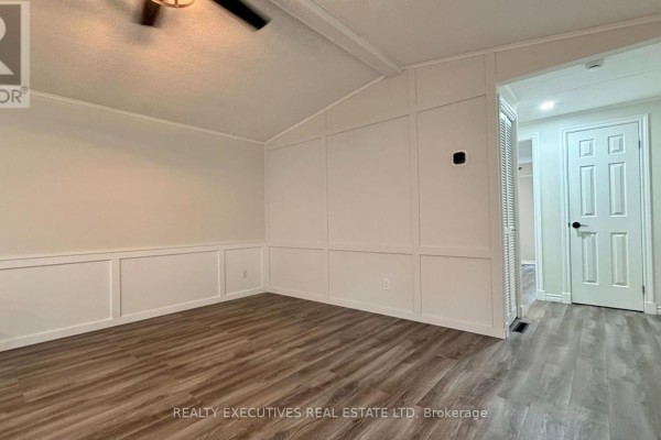 Empty living room space with wood-look flooring and white wainscoting on the walls. - 11 - 10146 County 43 Road, North Dundas