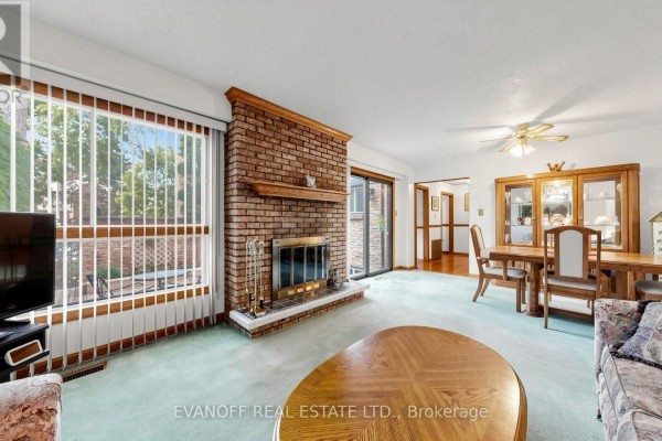 Living and dining room with a brick fireplace, large window, wooden furniture, and light blue carpet. - 11 - 117 Burrows Hall Boulevard, Toronto