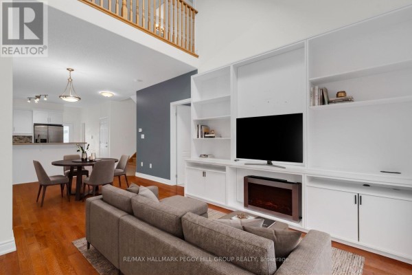 Living room with hardwood floors, a large sectional sofa, built-in white shelving, and a television. - 11 - 125 Huronia Road, Barrie