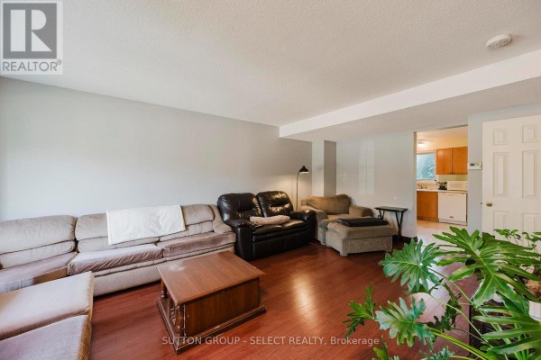 Living room with sectional sofa, dark wood floor, and an open doorway to a kitchen area. - 11 - 151 Martinet Avenue, London East