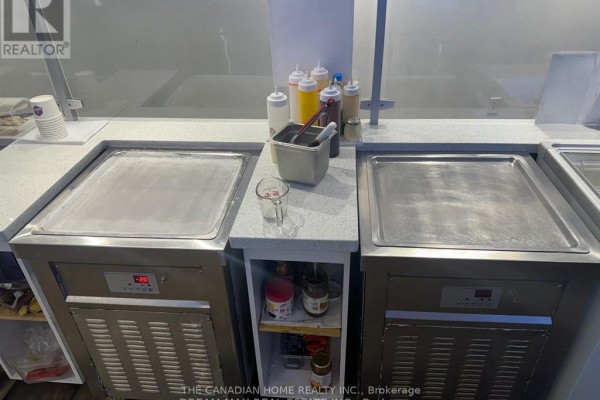 Close-up of two stainless steel ice cream rolling machines with containers of sauces on counter. - 11 - 511 Ray Lawson Boulevard E, Brampton