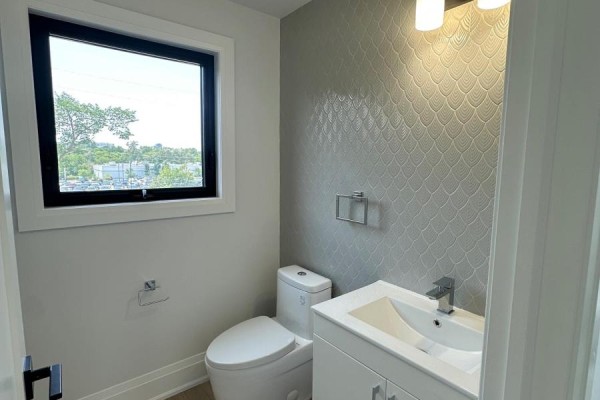 Powder room with a toilet, vanity, and a decorative tiled accent wall. - 11 - 59 Charles Street, Newmarket