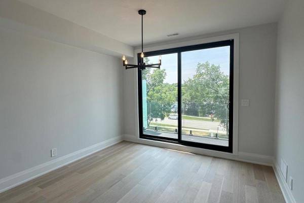 Empty room with light wood floors, a modern chandelier, and large sliding glass doors. - 11 - 59 Charles Street, Newmarket