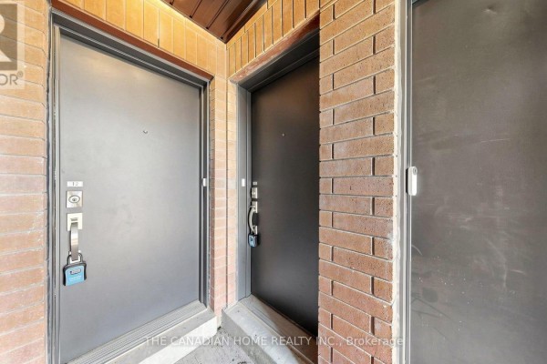 Two metal front doors with a brick wall on the right and a concrete walkway. - 11 - 65 Romilly Avenue, Brampton