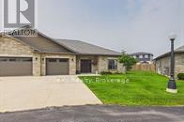 Front exterior view of a townhouse complex with concrete driveway and grass lawns. - 11-1050 Waterloo Street, Saugeen Shores
