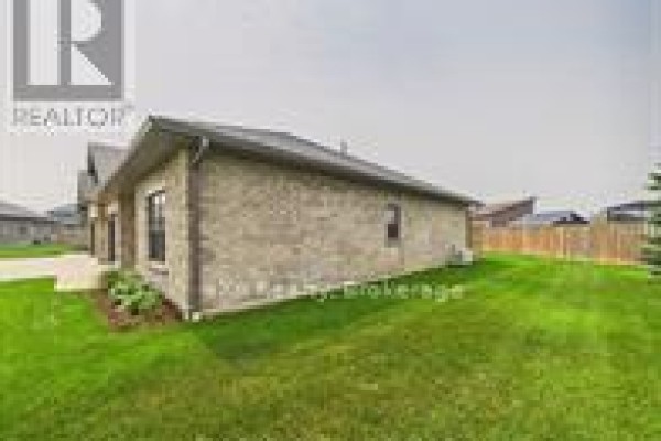 Side view of the townhouse showing brick exterior, windows, and green lawn. - 11-1050 Waterloo Street, Saugeen Shores