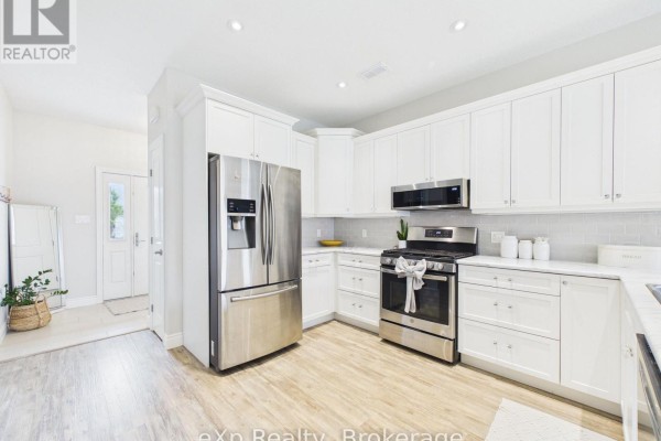 Bright white kitchen with stainless steel appliances, island, and light wood flooring. - 11-1050 Waterloo Street, Saugeen Shores