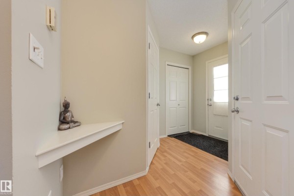 Interior foyer with light wood laminate flooring, a white corner shelf, and white doors. - #11 115 Chestermere Dr, Sherwood Park