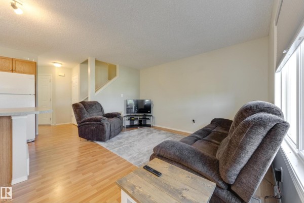 Living room with two recliners, a sofa, and a television next to a kitchen area. - #11 115 Chestermere Dr, Sherwood Park