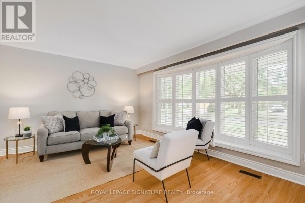 Living room with a grey sofa, two accent chairs, a coffee table, and a large bay window. - 11 Bellbury Crescent, Toronto