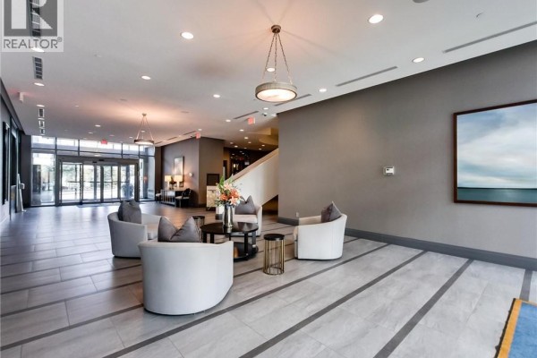 Lobby seating area with white curved sofas, round coffee tables, and modern art on gray walls. - 11 Bronte Road Unit# 306, Oakville