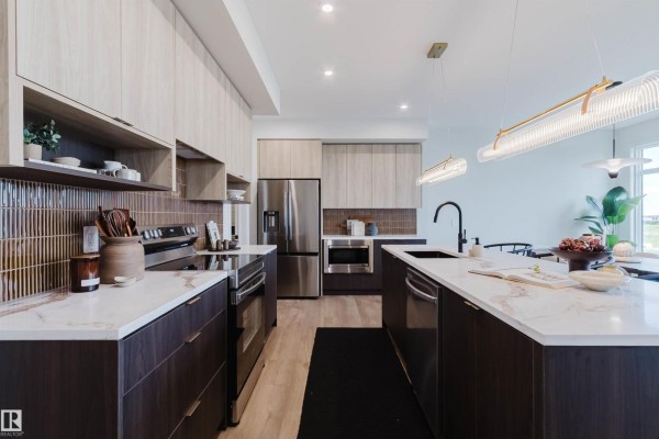Kitchen island with dark cabinets, white marble countertop, and black faucet, facing stainless steel appliances. - 11 Cessy St, St  Albert