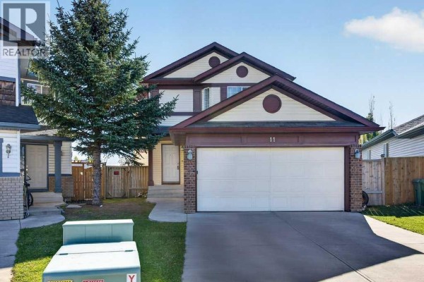Front exterior of a two-story house with a double garage door, beige siding, and dark red trim. - 11 Cimarron Meadows, Okotoks