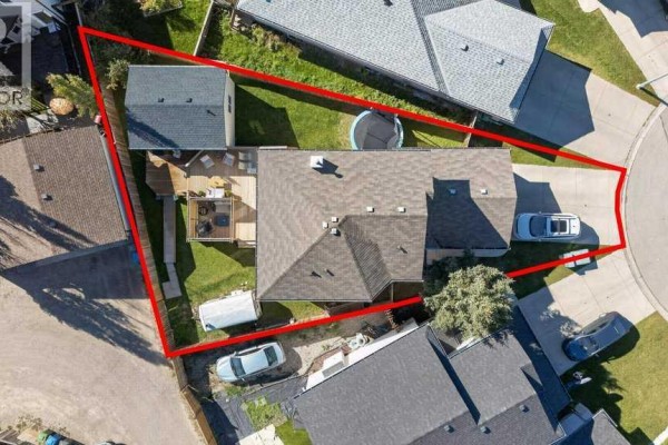 Overhead view of a house with a fenced backyard, featuring a deck, small shed, and green lawn. - 11 Cimarron Meadows, Okotoks