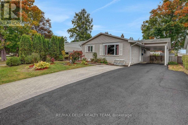 Side exterior view of a bungalow with a driveway, carport, and mature trees. - 11 Courtney Road, Ottawa