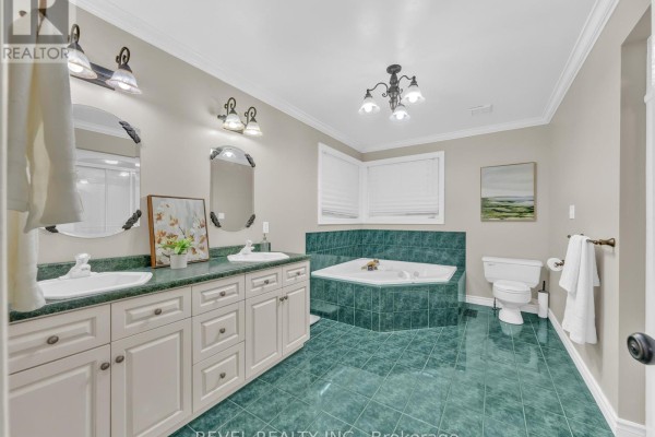 Spacious bathroom featuring a double vanity, corner jacuzzi tub with green tiled surround, and a toilet. - 11 Cramar Crescent, Chatham Kent
